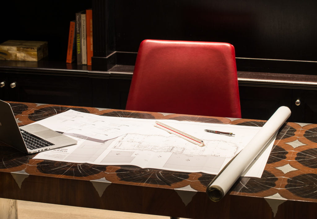 A red leather backed chair at a desk with architecture plans unrolled on the desk