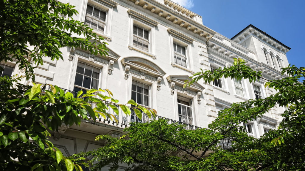 Upward view of a white, classical styled terrace house with a clear blue sky in the background