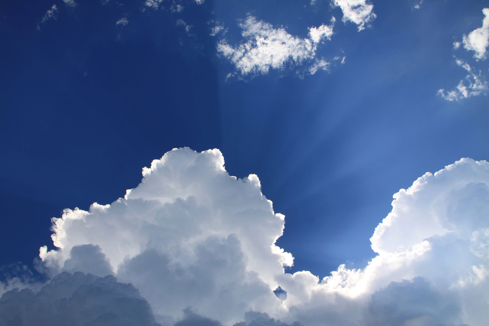 A bright blue sky with white clouds and the sun shining behind